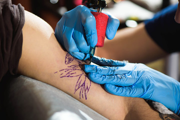 Master tattoo draws the black paint on the clients tattoo. Tattoo artist holding a tattoo machine...