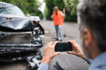 Unrecognizable man taking pictures of a broken car after an accident. - obrazy, fototapety, plakaty