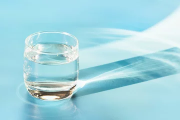 Fotobehang Glas water op pastelblauw. Een schot voor de tijd. Detailopname. Ruimte kopiëren. Waterbalans voor gezond. © svetlana_cherruty