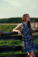 beautiful teenager girl with long healthy hair in blue dress relaxing on sunset evening in farm on summer time.