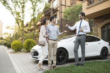 Happy young couple receiving car key from car salesperson