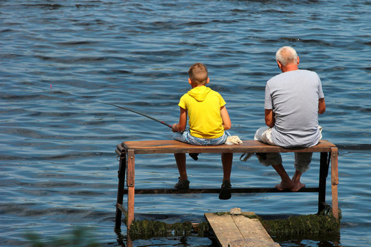 Old man and a boy sit on a self-made fishing platform with rods