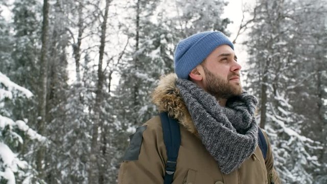 Happy young man looking around at beautiful winter nature in national park and then looking at camera and happily smiling