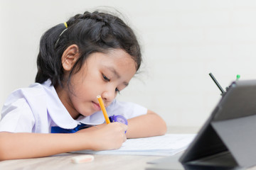 Asian little girl in student uniform doing homework on wooden table with tablet select focus shallow depth of field
