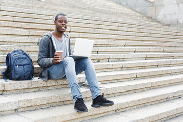 Handsome african-american man with laptop and coffee outdoors