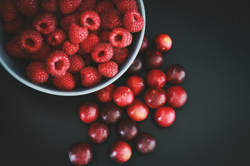 Raspberries and plums on a black table. Berries and fruit. 
