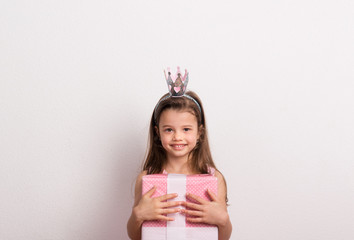 Portrait of a small girl with crown headband in studio, holding a wrapped box.