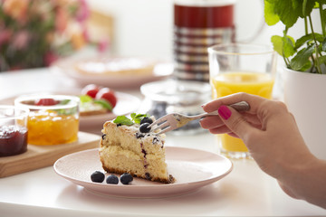 Homemade cake with blueberries on pastel pink plate placed on table with breakfast