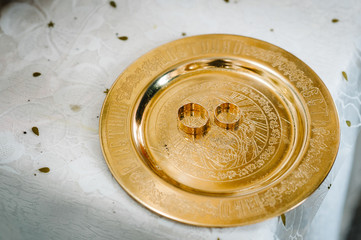 Two golden wedding rings in a plate on the table  at the ceremony before the wedding ceremony in the church.