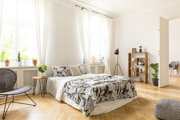 An interior of a bedroom with herringbone parquet, white walls and simple furniture. Bed, chair,...