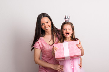 A small girl with crown headband and her mother holding a present in a studio.