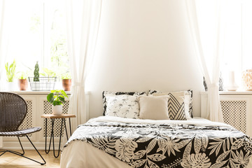 Close-up of leaf pattern black and white covers on a bed in a sunny bedroom interior. A rattan and...