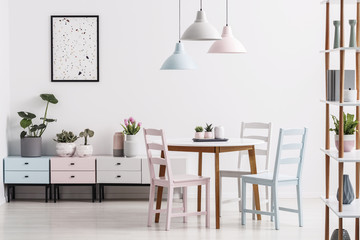 Real photo of a pastel dining room interior with a table, chairs, cabinets and poster