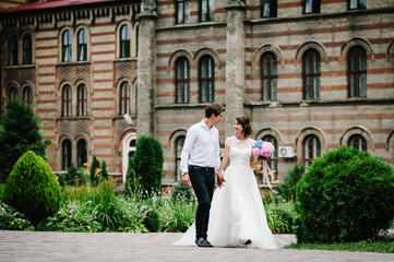 Portrait the groom in wedding suit and the bride in dress walking near ancient restored...