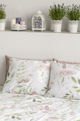 Real photo of wall shelf with fresh lavender, candles and decor above double bed with floral sheets