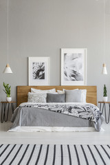 Posters on wooden headboard of bed with patterned blanket in grey bedroom interior with carpet....
