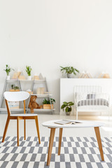 Table and chair on patterned carpet in white kid's bedroom interior with plants. Real photo