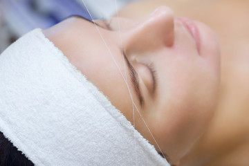 Obraz na płótnie Canvas The make-up artist plucks her eyebrows with a thread close-up. Face care beauty treatments in the beauty salon.