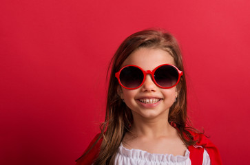 Portrait of a small girl with red sunglasses in studio on a red background.