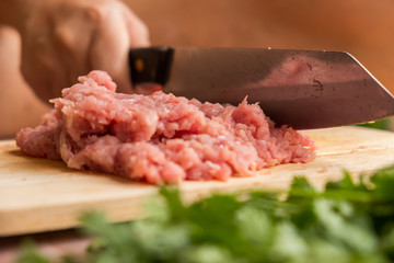 Chef is chopping the raw pork on the wooden cutting board with a sharp knife to cook in the kitchen.
