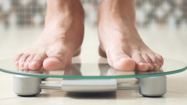 Male feet standing on electronic scales for weight control  on the bathroom.  Close-up . 