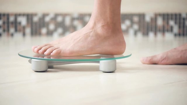 Male feet standing on electronic scales for weight control  on the bathroom. 