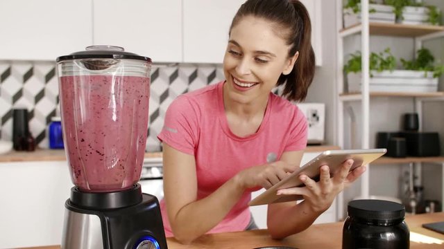 Woman using a tablet and preparing smoothie at kitchen