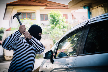 Thief wearing a black robe holding a hammer gunpoint robbery to steal a car.
