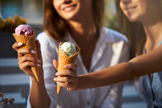 Close up shot of ice cream cones in hand of a woman standing with her friend. Two young women outdoors eating icecream on a sunny day. Isolated view, no face, copyspace for designers. Summer theme.