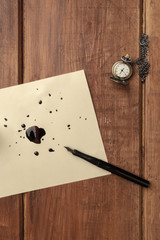 An overhead photo of a page with drops of ink, a nib pen, and a chain watch, with copy space, on a...