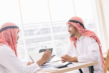 Two Arab business people working together in an office business project.He works on a laptop...
