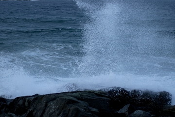 Spray from waves crashing into black rocks on rough day