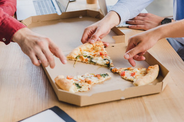 cropped shot of coworkers eating pizza at workplace