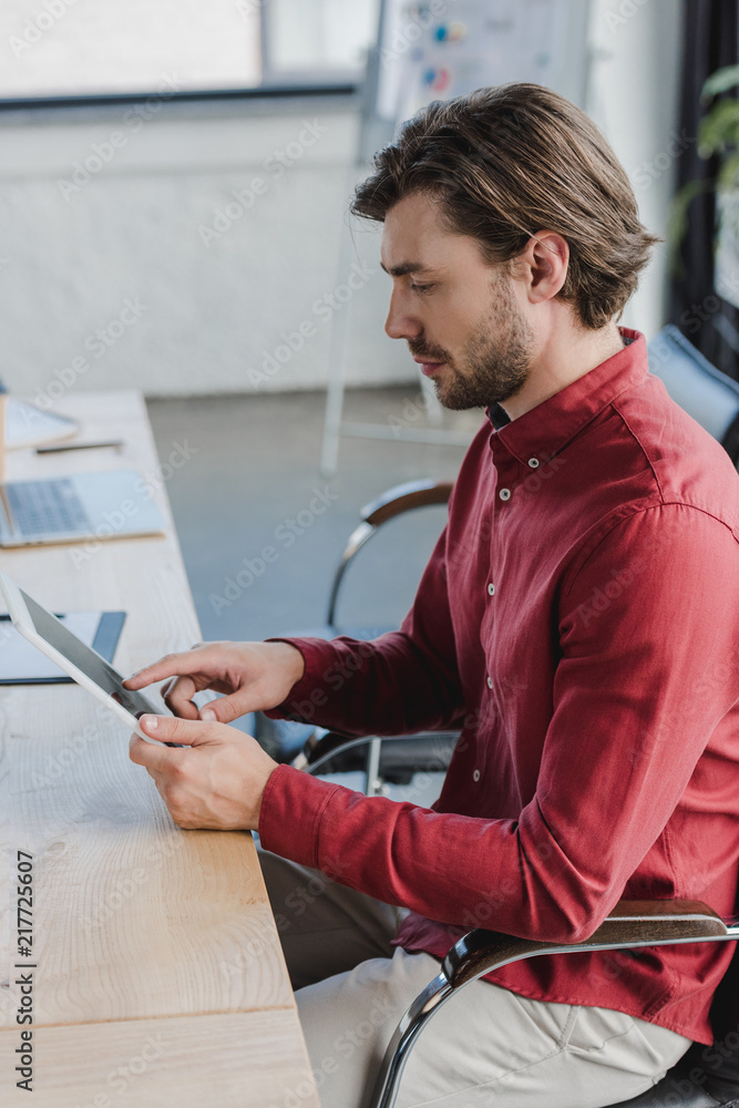 Wall mural side view of young businessman sitting and using digital tablet in office