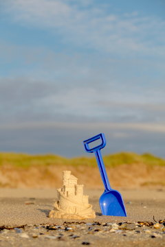 Small Toy Sand Castle On Beach With Blue Spade Behind And Dunes Space Above For Text