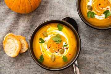 Pumpkin soup with pumpkin seeds on a bowl on linen textile background, top view. Autumn concept.