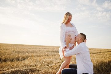 Obraz premium Pregnant couple in wreath field at white underwear clothes on sunset. Happy moments of pregnancy.