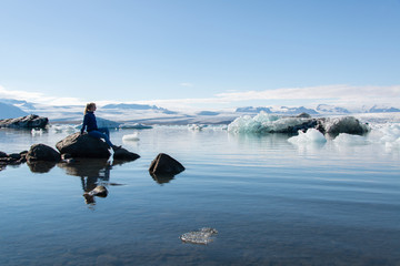 Island Gletschersee, junge Frau genießt auf Stein sitzend den Blick auf den Gletscher in der Abendsonne