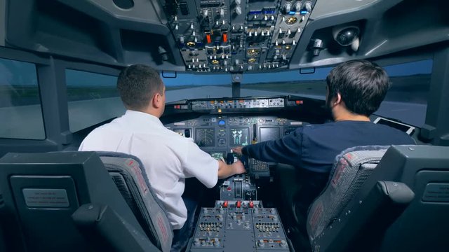 Two men are sitting in a cockpit of a flight simulator. Cockpit cabin flight deck.