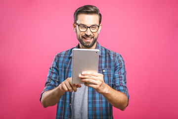 Happy young man in plaid shirt standing and using tablet over pink background