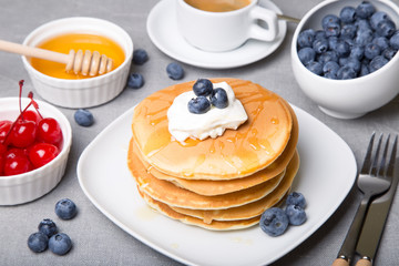 Pancakes with blueberries, cherries, sour cream, honey and coffee. Close-up. Selective focus.