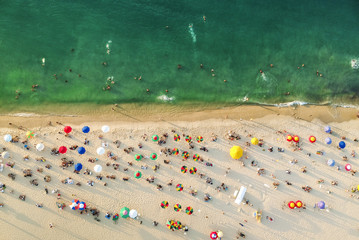 Aerial view of a beach with colorful umbrellas, people swimming in the sea, sunny day. Drone landscape from above