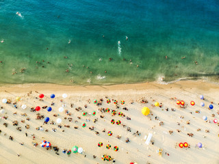 Aerial view of a beach with colorful umbrellas, people swimming in the sea, sunny day. Drone landscape from above