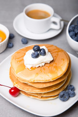 Pancakes with blueberries, cherries, sour cream, honey and coffee. Close-up. Selective focus.