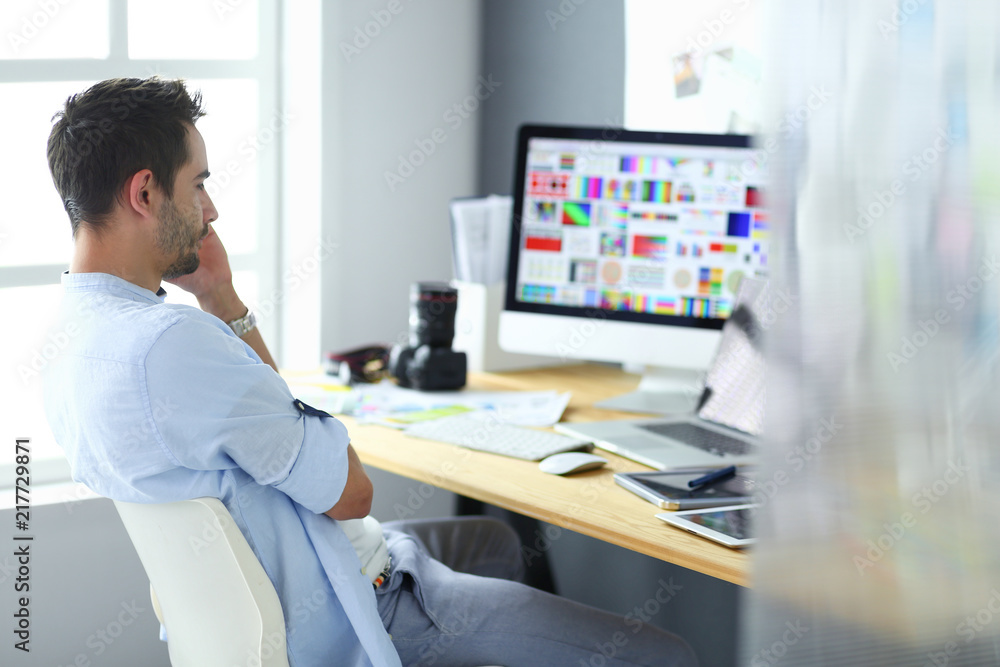 Poster portrait of young designer sitting at graphic studio in front of laptop and computer while working o