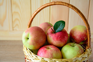 Wooden basket with red and green apples on front of brown wooden wall. Harvest concept