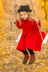 girl in a red coat swings on a swing and makes funny faces