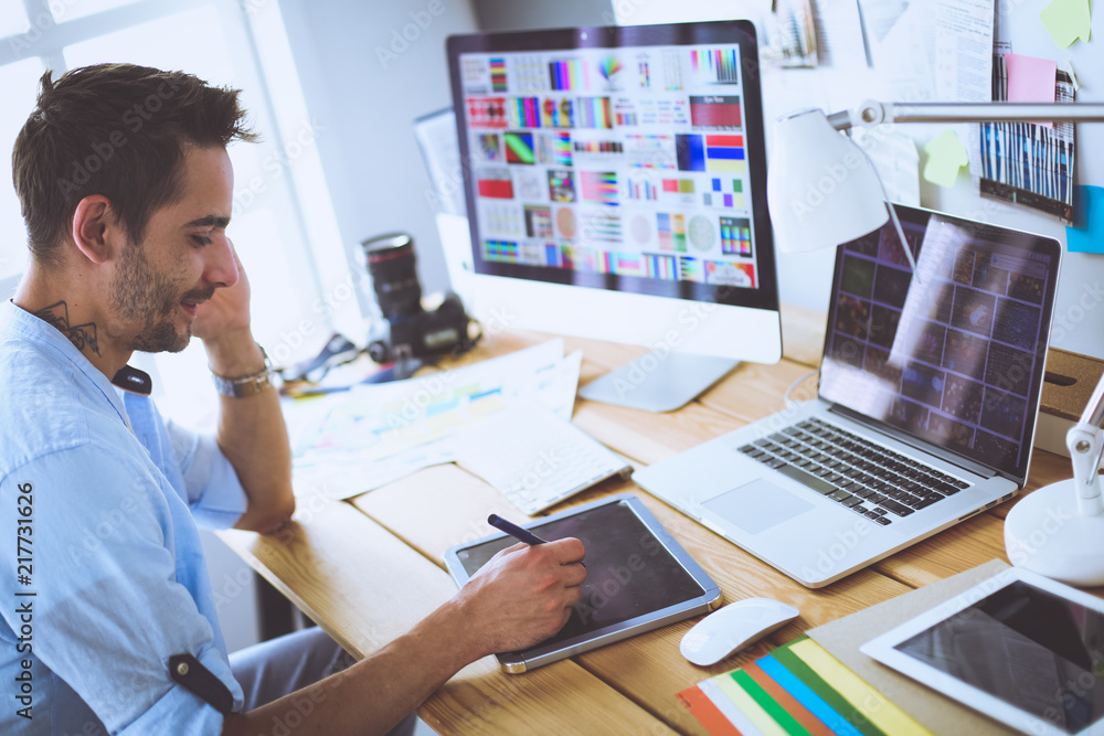 Poster portrait of young designer sitting at graphic studio in front of laptop and computer while working o