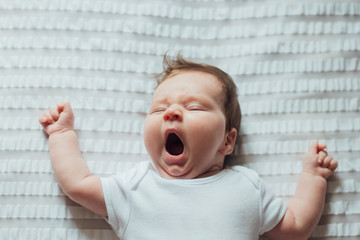 Infant baby sleeping and yawning on white sheets