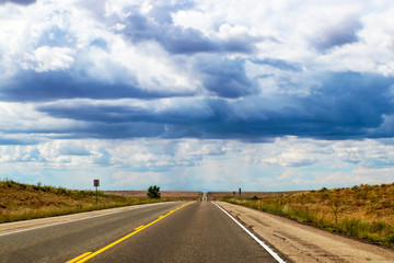 Road trip -Two lane highway on the plains stretches straight over horizonunder dramatic sky with strange light
